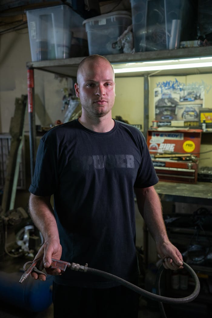 A mechanic holding an air blow gun in an industrial workshop setting.